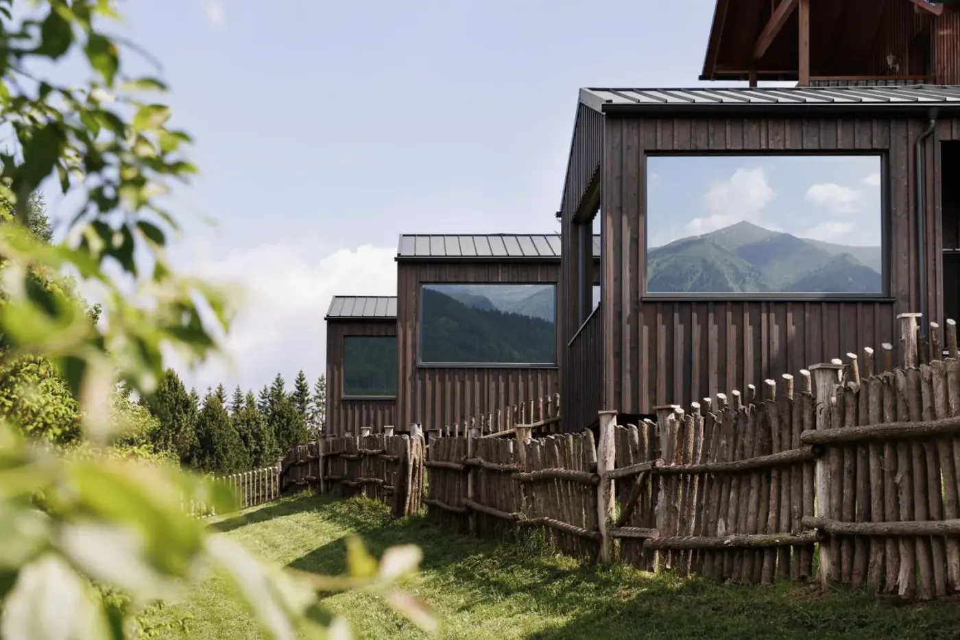 Timber cabins with large windows on a green hillside at Sloho Bergurlaub in Hohentauern, Austria.