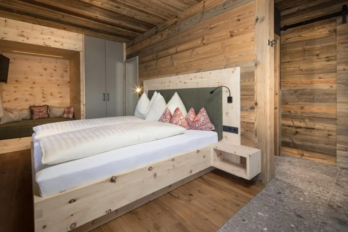 Double bedroom with rustic timber walls and a padded headboard at Stadl Lofts Plattenalm in Krimml, Austria.