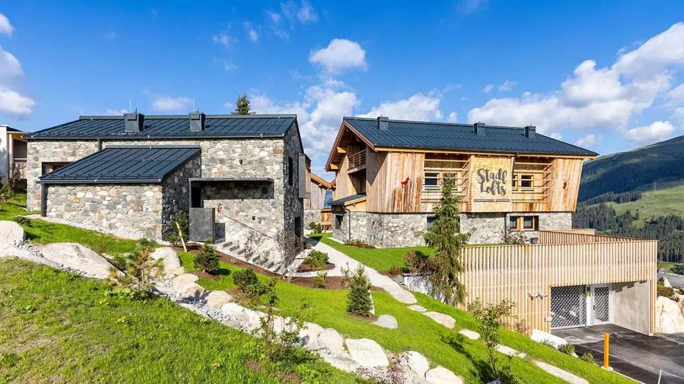 Timber-and-stone chalets beside a green mountain hillside at Stadl Lofts Plattenalm in Krimml, Austria.
